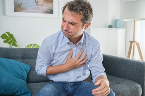 The man sitting on the sofa holding his chest is suffering from gastroesophageal reflux after eating